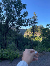 Load image into Gallery viewer, May include: A hand holds a long, thin incense stick in front of a scenic view of a forest with a blue sky in the background.