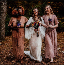 Load image into Gallery viewer, May include: Three women in a forest setting, wearing long, flowing dresses. The woman in the center is wearing a white lace dress and holding a bouquet of flowers. The women on either side are wearing brown and pink lace dresses. The women are smiling and walking together.