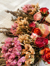 Load image into Gallery viewer, May include: A bundle of dried flowers and herbs featuring deep red roses, light pink statice, and sprigs of lavender. The arrangement is bound together with thin orange string and includes a small, light-colored rectangular wooden block.