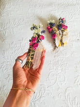 Load image into Gallery viewer, May include: A white crystal with dried flowers and herbs wrapped around it. The crystal is shaped like a point and is held in a hand.