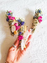 Load image into Gallery viewer, May include: Three bundles of dried herbs and flowers tied with twine and wrapped around clear quartz crystals. The bundles are made with lavender, rosemary, and other dried flowers. The bundles are held in a hand.