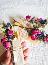 Load image into Gallery viewer, May include: A bundle of dried herbs and flowers tied with twine, with clear quartz crystals wrapped in twine and tied to the bundle. The bundle is held in a hand.