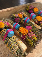 Load image into Gallery viewer, May include: Several bundles of dried herbs and palo santo wood sticks wrapped with yellow string. Each bundle is decorated with a bright blue stone secured by pink thread, a dried orange rose, a dried pink rose, and small yellow flowers.
