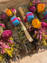 Load image into Gallery viewer, May include: Three bundles of dried herbs and palo santo wood sticks wrapped in yellow twine. Each bundle is decorated with dried yellow and pink roses, yellow wildflowers, and a single blue turquoise-colored stone secured with bright pink thread.