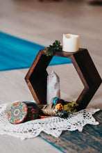 Load image into Gallery viewer, May include: A dark brown wooden hexagonal shelf holding a white LED candle and a small green sprig on top. Inside the shelf sits a tall, light-colored crystal point. Beside the shelf is a small round tin with a colorful floral pattern and a bundle of dried flowers tied with twine.