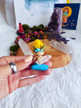 Load image into Gallery viewer, May include: A small, yellow-haired troll figurine with turquoise gemstone accents, standing on a clear quartz crystal and a turquoise stone.