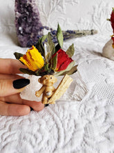 Load image into Gallery viewer, May include: A small plastic troll figurine with a yellow and red flower crown, a clear crystal, and a wooden stick on a white crystal rock.