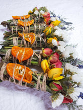 Load image into Gallery viewer, May include: A collection of dried orange slices and flowers bundled together with twine. The bundles are arranged in a row on a white surface.