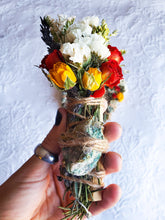 Load image into Gallery viewer, May include: A smudge stick with dried flowers, herbs, and a green crystal wrapped in twine. The flowers include white, yellow, and red roses.