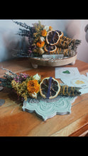 Load image into Gallery viewer, May include: Two bundles of dried herbs and flowers with dried citrus slices. The bundles are tied with twine and are sitting on a decorative wooden and a concrete base. The bundles are labeled "Lemon" and "Protection, Prosperity, Abundance, The Money Plant, Success".
