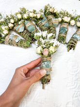 Load image into Gallery viewer, May include: A collection of smudge sticks with dried flowers and green crystals wrapped in twine. The smudge sticks are tied with twine and have a green crystal in the center. The smudge sticks are on a white surface.