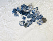 Load image into Gallery viewer, May include: A collection of blue and white sodalite rough stones. The stones are various sizes and shapes. A US quarter is included for size reference.
