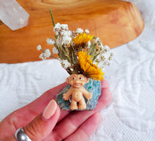 Load image into Gallery viewer, May include: A small, brown troll figurine with a green and blue stone base. The troll is surrounded by a bouquet of yellow and white flowers.
