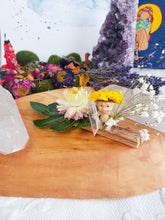 Load image into Gallery viewer, May include: A small wooden figurine of a person with a yellow flower crown sits on a wooden surface with a clear quartz crystal, dried flowers, and a piece of driftwood.
