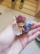 Load image into Gallery viewer, May include: A small plastic troll figurine wearing a dried pink rose on its head. The troll is holding a clear quartz crystal and is sitting on a purple amethyst crystal.

