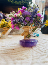 Load image into Gallery viewer, May include: A small, beige troll figurine holding a bouquet of dried flowers in shades of purple, pink, and white. The flowers are arranged on a purple amethyst stone.
