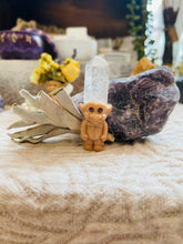 Load image into Gallery viewer, May include: A small brown troll figurine with a clear quartz crystal on its head. The troll is standing on a white cloth surface with a purple amethyst rock behind it.
