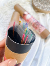 Load image into Gallery viewer, May include: A cardboard tube with a black lid containing a variety of colorful incense sticks. The sticks are packaged in individual clear plastic sleeves.
