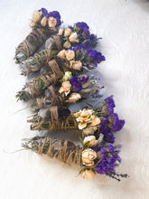 Load image into Gallery viewer, May include: A set of five smudge sticks wrapped in twine and decorated with dried flowers. The flowers are a mix of purple and cream colors. The smudge sticks are tied with twine and have a crystal at the end.
