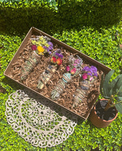 Load image into Gallery viewer, May include: A set of four smudge sticks with dried flowers and crystals in a brown box. The smudge sticks are wrapped in twine and have different colored flowers and crystals.
