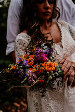 Load image into Gallery viewer, May include: A bride holds a bouquet of colorful flowers, including orange, red, purple, and yellow blooms. The bouquet is arranged in a rustic style with greenery and dried elements.
