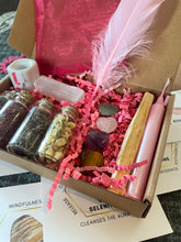 Load image into Gallery viewer, May include: A pink and brown gift box filled with various items, including crystals, herbs, a feather, a candle, and incense sticks. The box is open and the items are visible. The box is labeled with the words "Selenite Cleanses the Aura".

