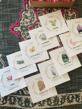 Load image into Gallery viewer, May include: A set of eight white cards with gold trim, each featuring a different crystal or herb and its associated properties. The cards include Amethyst, Rose Quartz, Aventurine, Selenite, Tiger's Eye, Rosemary, Palo Santo, and Lavender.
