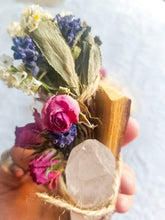 Load image into Gallery viewer, May include: A small bundle of dried flowers and herbs tied with twine, including lavender, white flowers, and pink roses. A clear quartz crystal is attached to the bundle, and a piece of wood is visible behind the flowers.
