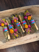 Load image into Gallery viewer, May include: Four bundles of dried herbs and wood sticks wrapped in yellow twine. Each bundle features a bright blue stone secured with pink thread, accented with dried yellow roses, pink rosebuds, and small yellow and purple wildflowers.
