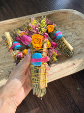 Load image into Gallery viewer, May include: A bundle of dried herbs and palo santo wood sticks wrapped with yellow string, featuring a bright blue stone secured by pink thread, adorned with dried yellow and pink flowers, including roses, and small sprigs of greenery.
