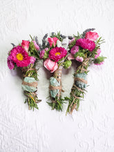 Load image into Gallery viewer, May include: Three bundles of dried herbs and flowers tied with twine and wrapped around a green stone. The bundles are arranged in a row on a white surface.
