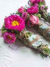 Load image into Gallery viewer, May include: Three bundles of dried herbs and flowers tied with twine. The bundles are made with rosemary, lavender, and pink flowers. The bundles are tied with twine and have a green stone in the center.
