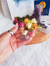 Load image into Gallery viewer, May include: A small, plastic troll figurine holding a bouquet of dried flowers tied with twine. The flowers are a mix of pink, yellow, and white roses, and other dried flowers. The bouquet is sitting on a small, round, purple and brown stone.
