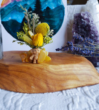 Load image into Gallery viewer, May include: A small yellow plastic troll figurine with dried flowers in its hair. The troll is sitting on a wooden base with yellow crystals.

