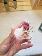Load image into Gallery viewer, May include: A small pink troll doll figurine with a dried pink rose and white baby's breath flowers on its head. The troll is sitting on a large, pink, rose quartz crystal.
