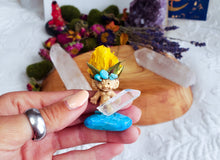 Load image into Gallery viewer, May include: A small troll figurine with yellow flower hair, turquoise gemstone eyes, and a clear quartz surfboard. The troll is standing on a turquoise stone.

