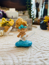 Load image into Gallery viewer, May include: A small troll figurine with a blue and brown flower crown, holding a clear quartz crystal, standing on a blue turquoise stone.
