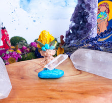Load image into Gallery viewer, May include: A small troll figurine wearing a yellow flower crown and turquoise beads, holding a clear quartz crystal and standing on a turquoise blue stone.
