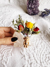 Load image into Gallery viewer, May include: A small plastic troll doll with a red and white hat sits on a clear quartz crystal. The troll is surrounded by a bouquet of dried flowers, including yellow, red, and white roses.
