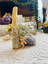Load image into Gallery viewer, May include: A small, light brown troll figurine with a white flower bouquet on its head, standing next to a white palo santo stick and a purple amethyst crystal.
