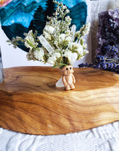 Load image into Gallery viewer, May include: A small, brown troll figurine with white flowers and clear quartz crystals in its hair. The troll is sitting on a wooden surface.
