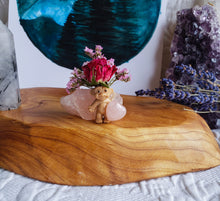 Load image into Gallery viewer, May include: A small, brown troll doll figurine holding a pink heart-shaped crystal. The troll is surrounded by pink and white flowers and a pink crystal rock. The figurine is sitting on a wooden surface.
