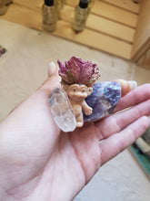 Load image into Gallery viewer, May include: A small plastic troll figurine wearing a dried pink rose on its head. The troll is holding a clear quartz crystal and is sitting on a purple amethyst crystal.
