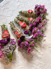 Load image into Gallery viewer, May include: Several bundles of dried herbs and flowers are arranged on a white surface. Each bundle is wrapped with twine and adorned with dried strawberries and purple flowers. The bundles are a mix of green, purple, and red.
