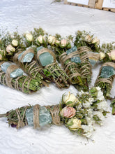 Load image into Gallery viewer, May include: A collection of smudge sticks with dried flowers and green crystals. The smudge sticks are wrapped in twine and tied with a bow. The flowers are white and pink. The crystals are green and have a rough texture.
